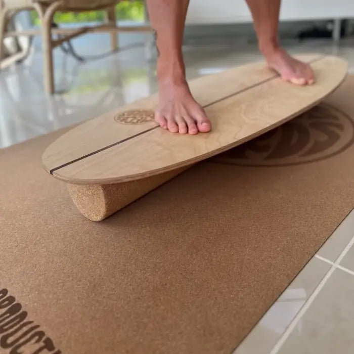 Person trainiert barfuss auf dem Balance Board mit Korkrolle auf einer Korkmatte im Innenbereich.