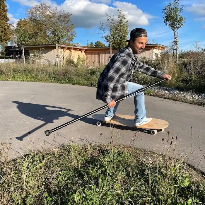 Fahrer surft mit dem Land-Surfer Longboard und Paddle über den Asphalt