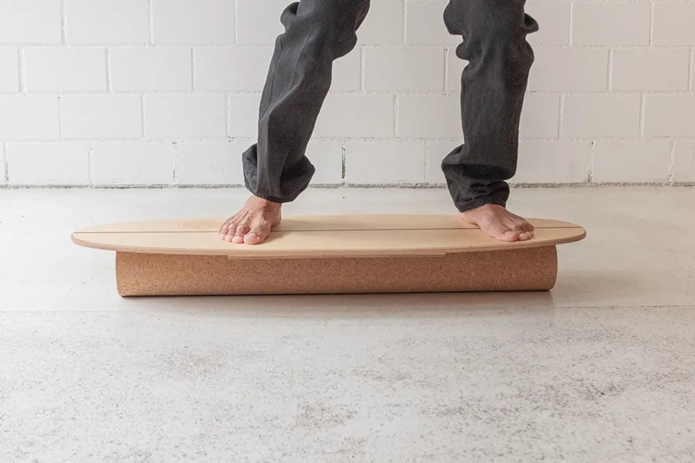 Person trainiert barfuss auf einem Balance Board von Mecos Board mit fester Korkrolle auf hellem Untergrund