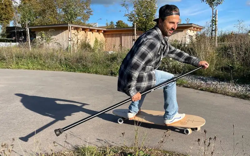 Fahrer surft mit dem Land-Surfer Longboard und Paddle über den Asphalt