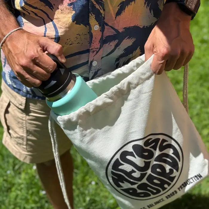 Person packt eine Trinkflasche in den Daily Cotton Bag von Mecos Boards – nachhaltiger Baumwollbeutel mit Retro-Logo.