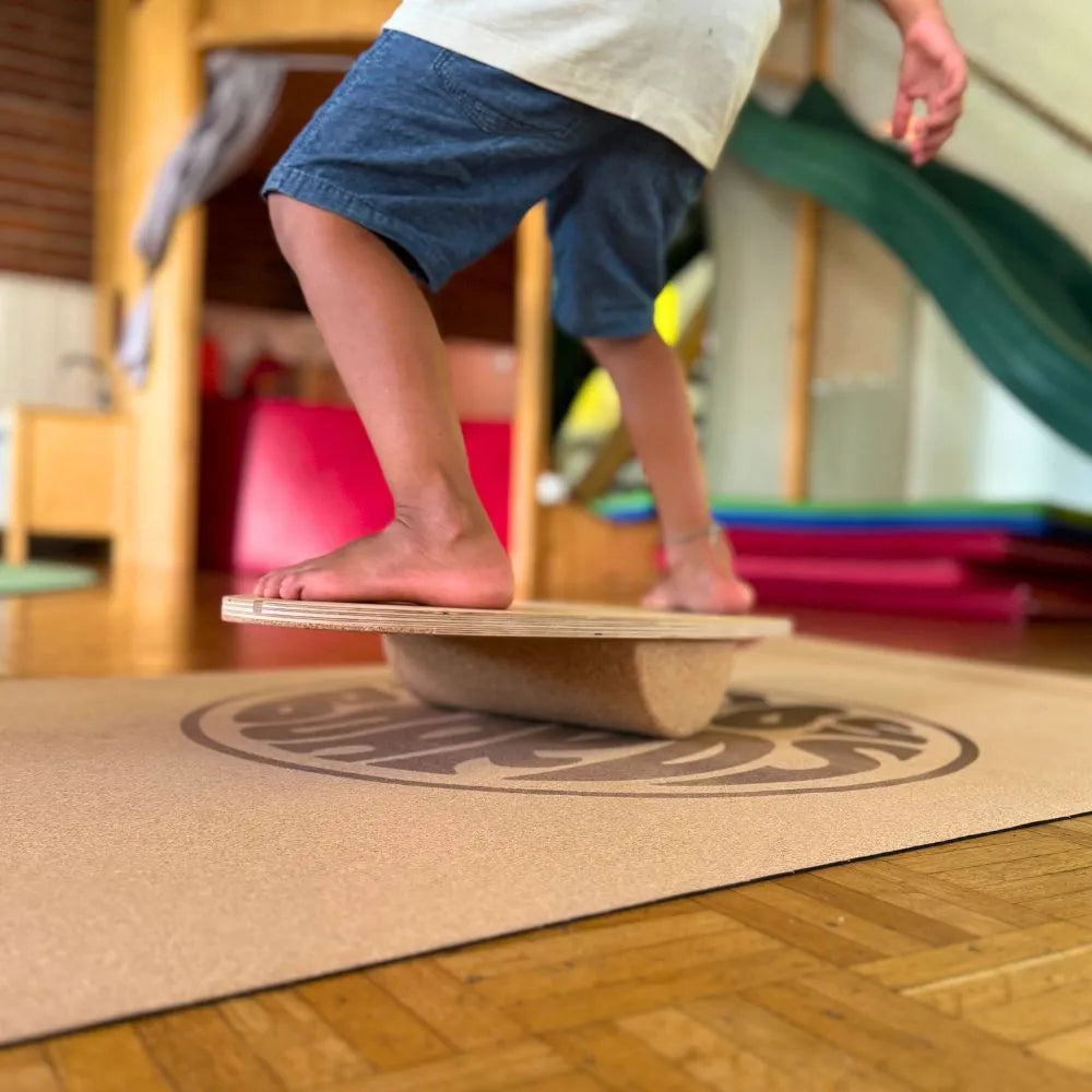 Kind balanciert sicher auf Mini Balance Board mit Korkrolle im Wohnzimmer