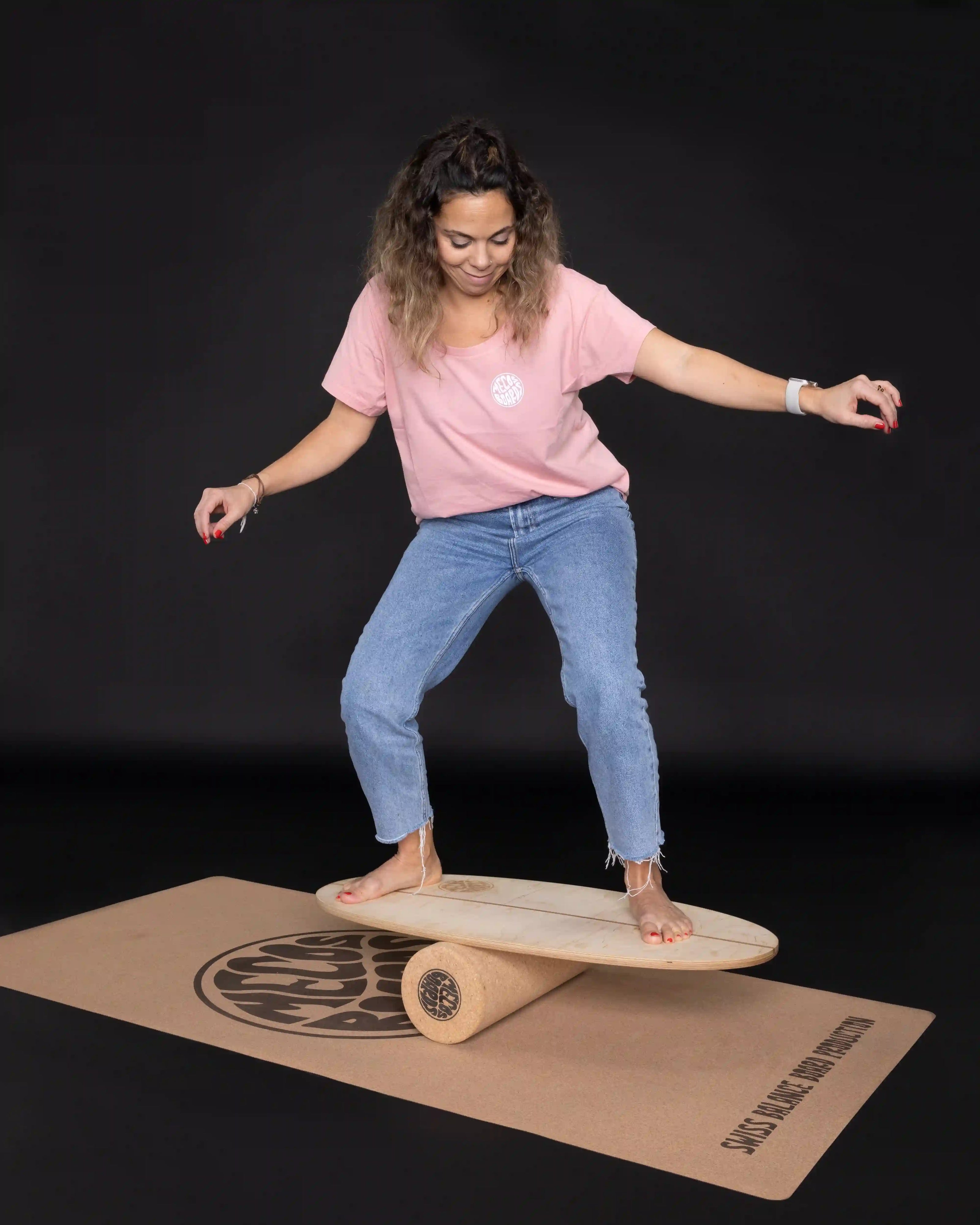 Frau balanciert auf dem MECOS BOARDS THE SHORTY Balance Board mit Korkrolle und Korkmatte.